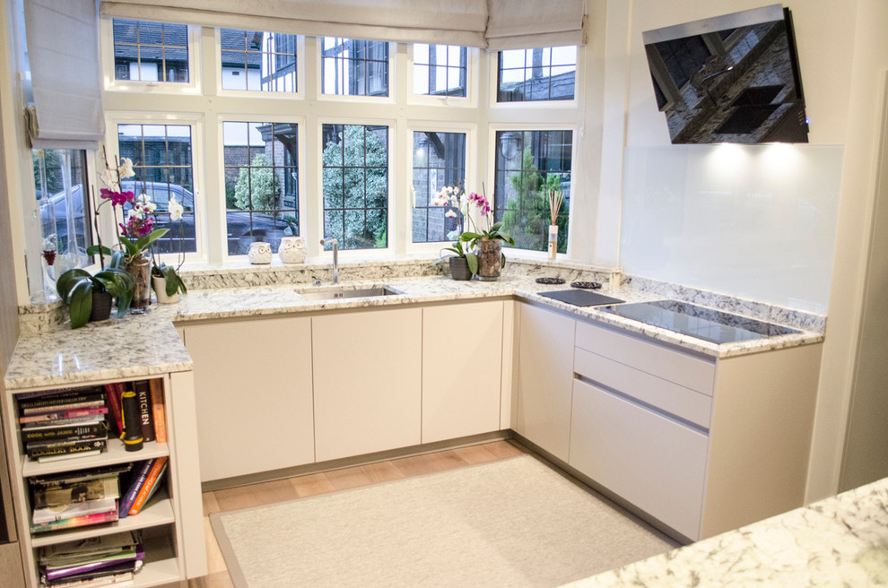 Large contemporary u-shaped open plan kitchen in London with a submerged sink, flat-panel cabinets, white cabinets, granite worktops, glass sheet splashback, black appliances and an island.