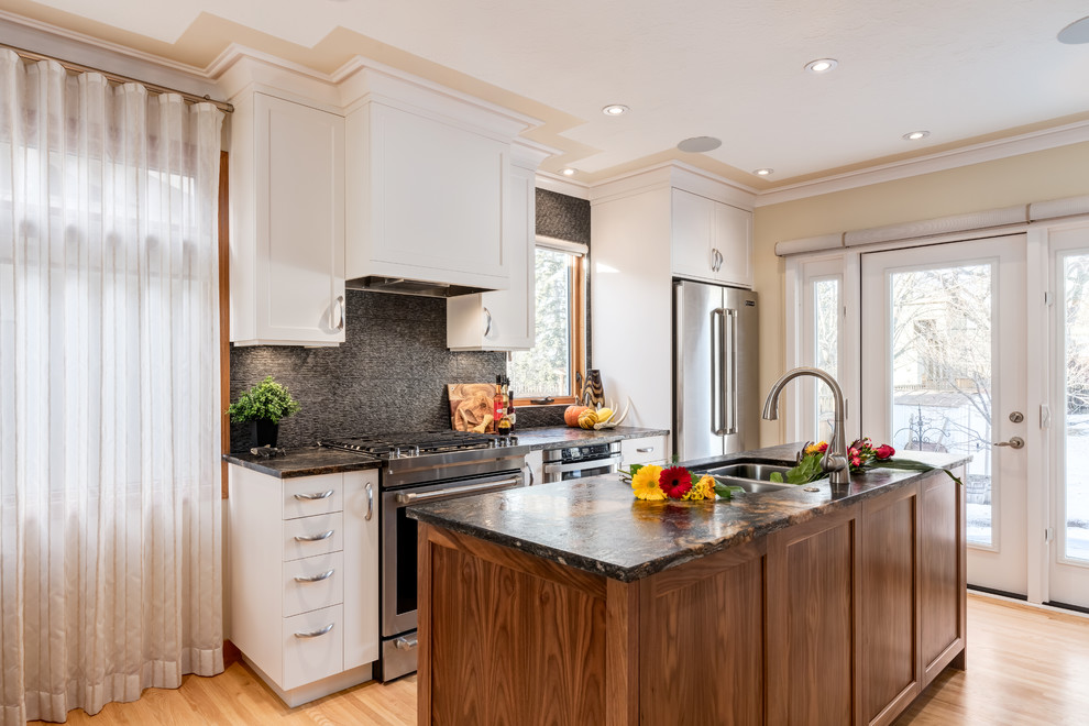 Photo of a traditional galley kitchen/diner in Calgary with a submerged sink, shaker cabinets, white cabinets, granite worktops, grey splashback, porcelain splashback, stainless steel appliances, light hardwood flooring and an island.