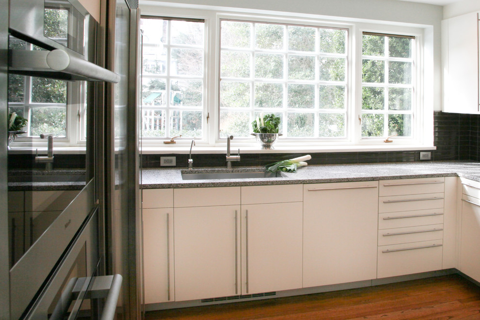 Diseño de cocinas en U actual de tamaño medio con armarios con paneles lisos, puertas de armario blancas, encimera de cuarzo compacto, salpicadero negro y salpicadero de azulejos de vidrio