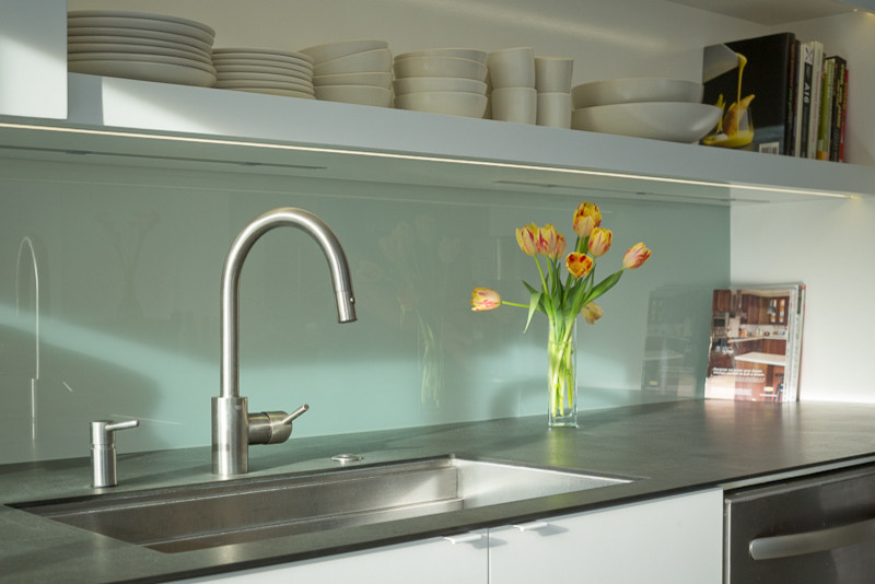 Example of a mid-century modern galley eat-in kitchen design in San Francisco with an undermount sink, flat-panel cabinets, white cabinets, white backsplash, glass sheet backsplash and stainless steel appliances