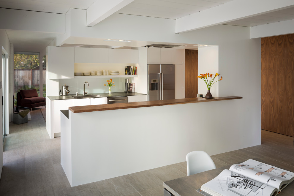 Medium sized midcentury galley kitchen/diner in San Francisco with a submerged sink, flat-panel cabinets, white cabinets, glass sheet splashback, stainless steel appliances, composite countertops, porcelain flooring, beige floors, black worktops and exposed beams.