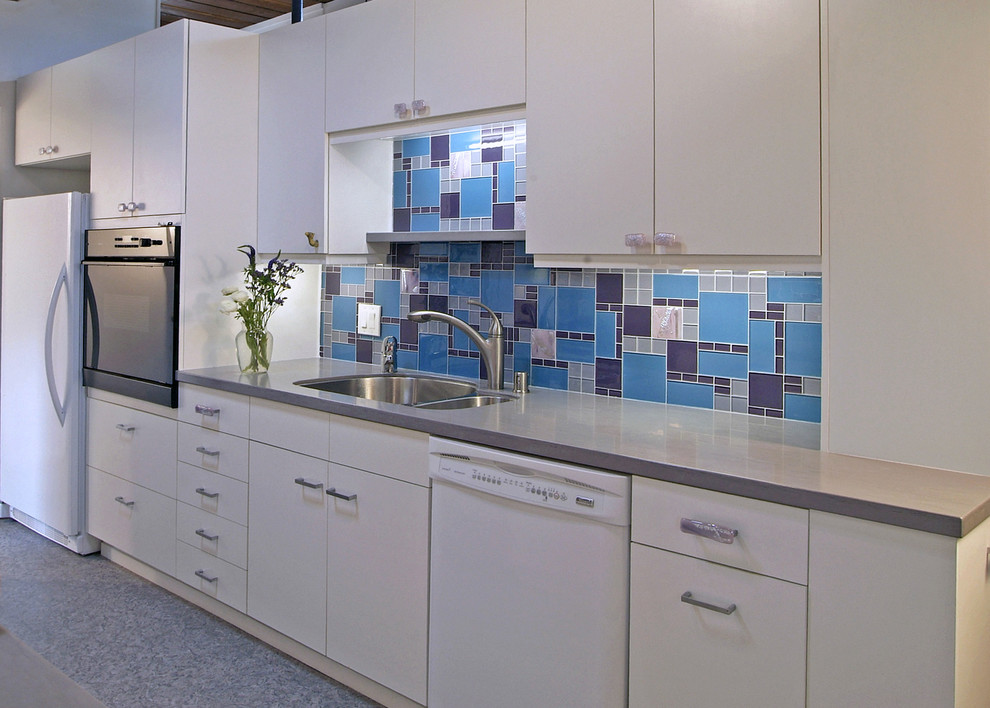 Example of a trendy kitchen design in Omaha with a double-bowl sink, white appliances, flat-panel cabinets, white cabinets, multicolored backsplash and glass tile backsplash
