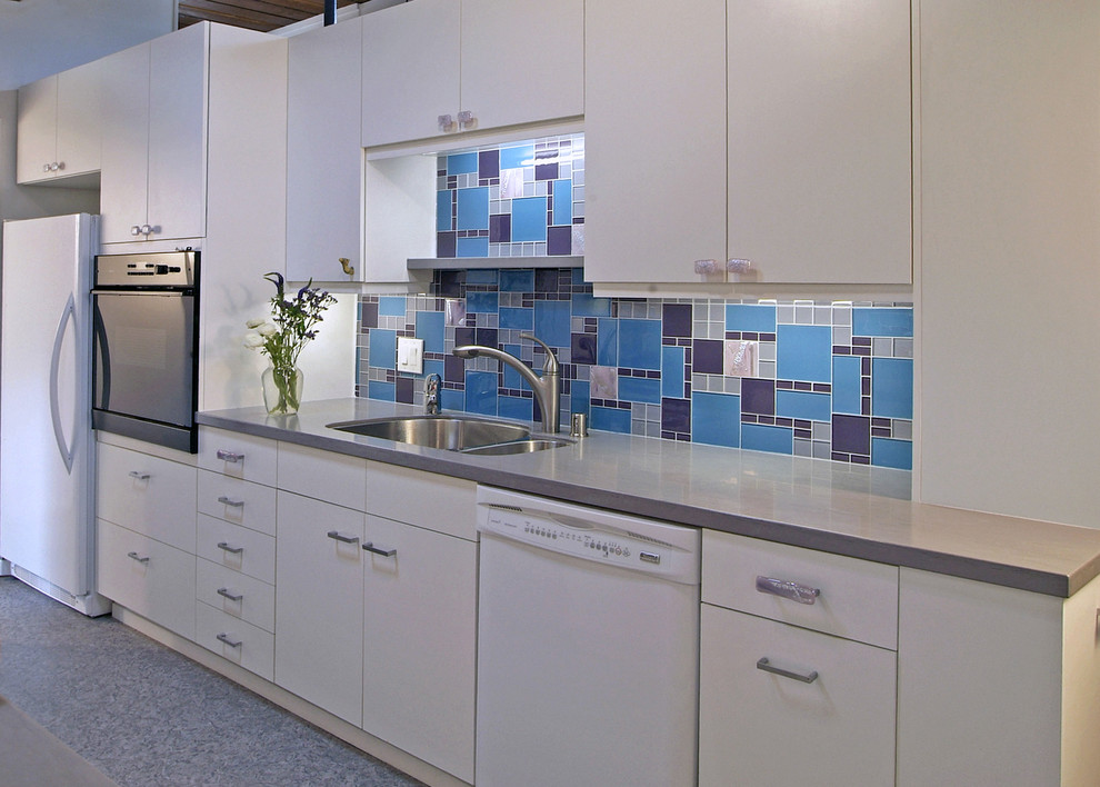 Cette image montre une cuisine design avec un évier 2 bacs, un électroménager blanc, un placard à porte plane, des portes de placard blanches, une crédence multicolore et une crédence en carreau de verre.