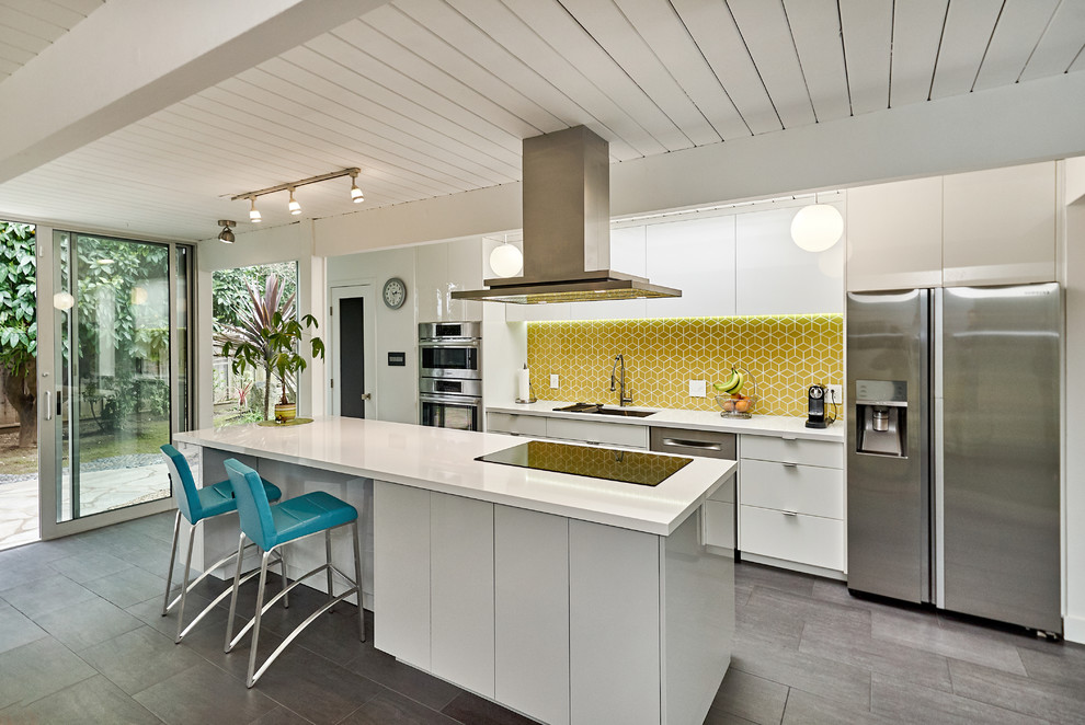 Immagine di un cucina con isola centrale minimalista con lavello sottopiano, ante lisce, ante bianche, paraspruzzi giallo, elettrodomestici in acciaio inossidabile, pavimento grigio e top bianco