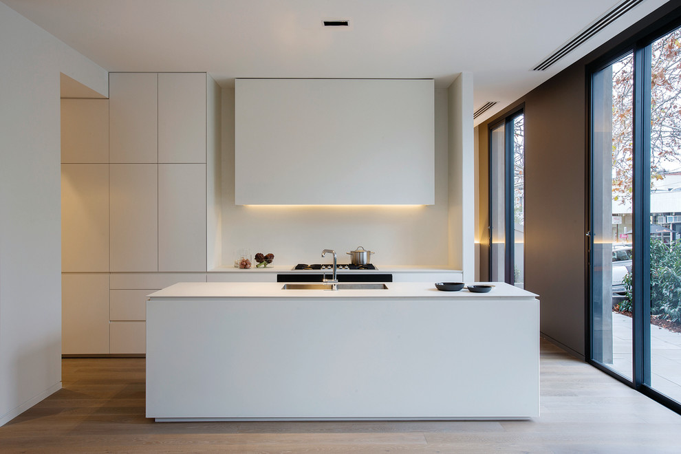 Zweizeilige, Mittelgroße Moderne Küche mit Unterbauwaschbecken, flächenbündigen Schrankfronten, weißen Schränken, Küchenrückwand in Weiß, braunem Holzboden, Kücheninsel und Glasrückwand in Melbourne