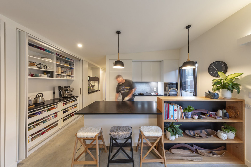 Zweizeilige, Kleine Moderne Wohnküche mit flächenbündigen Schrankfronten, weißen Schränken, Küchenrückwand in Grau, Rückwand aus Keramikfliesen, Küchengeräten aus Edelstahl, Betonboden, Kücheninsel, grauem Boden und schwarzer Arbeitsplatte in Canberra - Queanbeyan