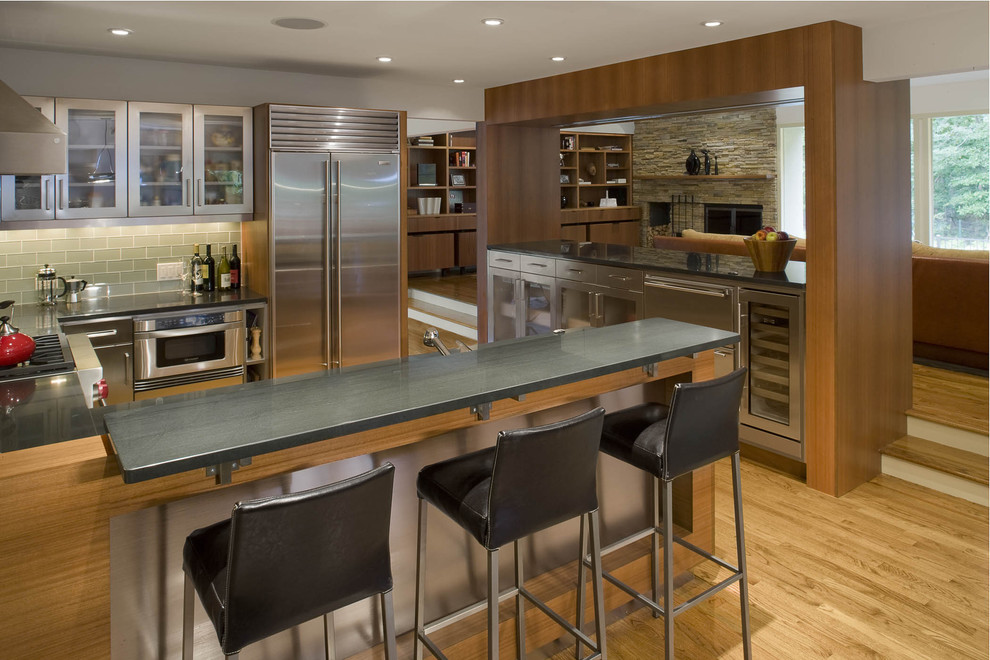 This is an example of a contemporary u-shaped kitchen in New York with metro tiled splashback, glass-front cabinets, green splashback and stainless steel appliances.