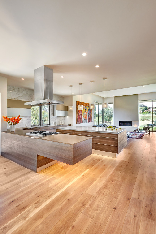 Example of a large trendy u-shaped light wood floor open concept kitchen design in Sacramento with an undermount sink, flat-panel cabinets, gray cabinets, quartz countertops, gray backsplash, stone tile backsplash, paneled appliances and two islands