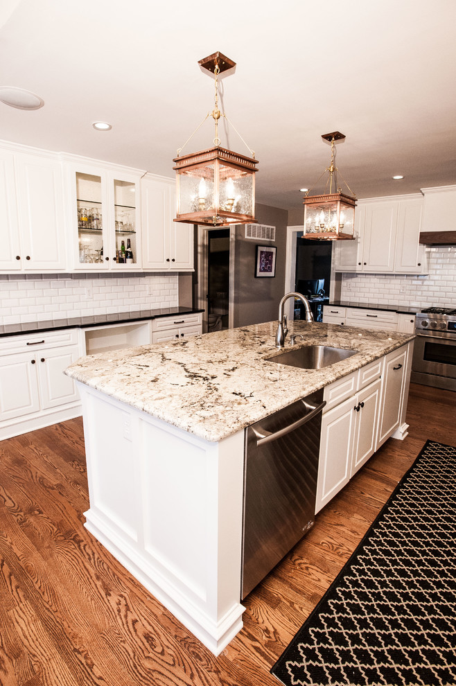 Cette photo montre une cuisine linéaire chic avec des portes de placard blanches, un plan de travail en granite, une crédence blanche, un électroménager en acier inoxydable, un sol en bois brun et îlot.