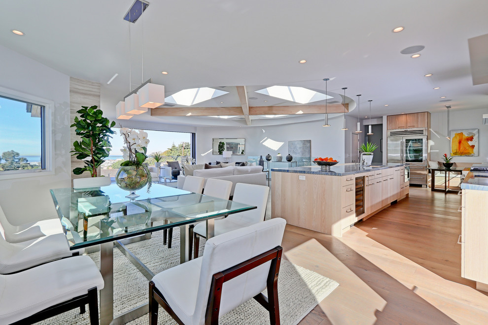 This is an example of a large contemporary open plan kitchen in Los Angeles with a built-in sink, flat-panel cabinets, light wood cabinets, quartz worktops, white splashback, glass tiled splashback, stainless steel appliances, light hardwood flooring and an island.