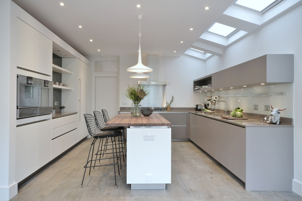 Inspiration for a medium sized contemporary l-shaped kitchen/diner in London with a submerged sink, flat-panel cabinets, grey cabinets, glass sheet splashback, an island and grey floors.
