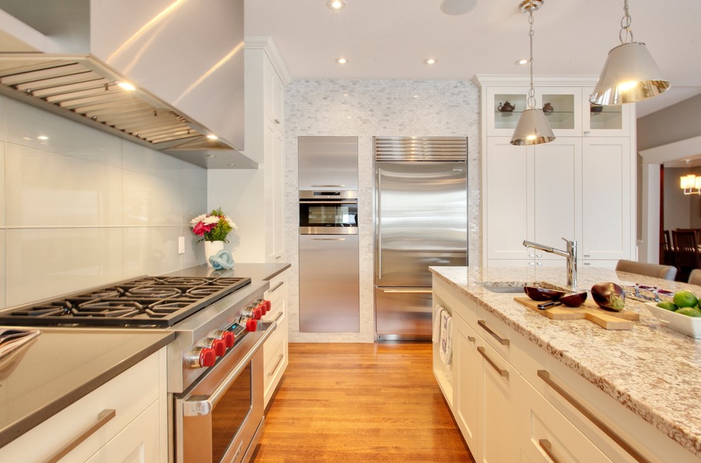 This is an example of a medium sized classic u-shaped open plan kitchen in Calgary with a submerged sink, shaker cabinets, white cabinets, granite worktops, white splashback, glass sheet splashback, stainless steel appliances, medium hardwood flooring, an island and brown floors.