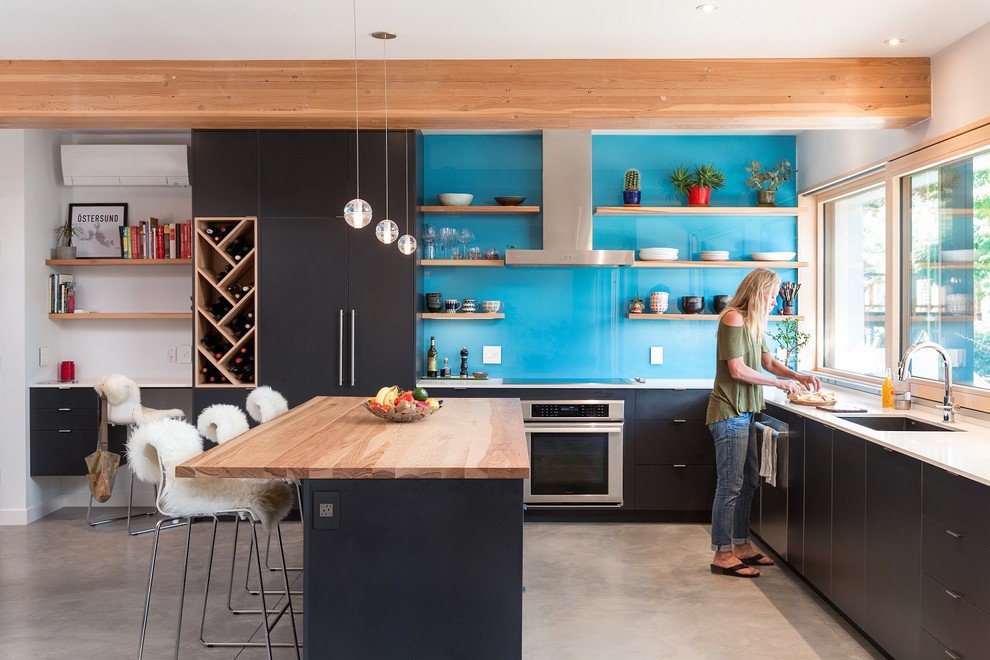 Moderne Küche in L-Form mit Unterbauwaschbecken, flächenbündigen Schrankfronten, schwarzen Schränken, Küchenrückwand in Blau, Küchengeräten aus Edelstahl, Betonboden, Kücheninsel, grauem Boden und weißer Arbeitsplatte in Denver