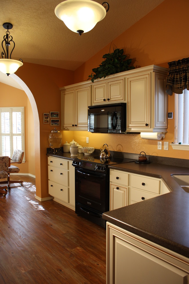 Klassisk inredning av ett stort brun brunt kök, med en integrerad diskho, luckor med upphöjd panel, vita skåp, bänkskiva i koppar, grått stänkskydd, svarta vitvaror, mellanmörkt trägolv och brunt golv