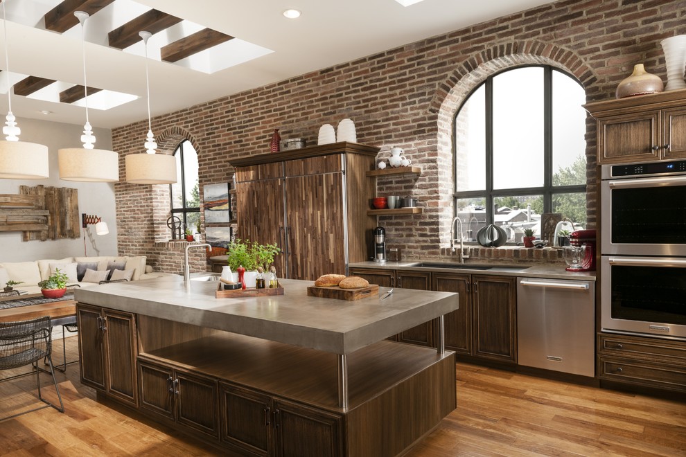 Inspiration for a transitional medium tone wood floor open concept kitchen remodel in San Diego with an undermount sink, recessed-panel cabinets, dark wood cabinets, concrete countertops, red backsplash, brick backsplash, paneled appliances and an island