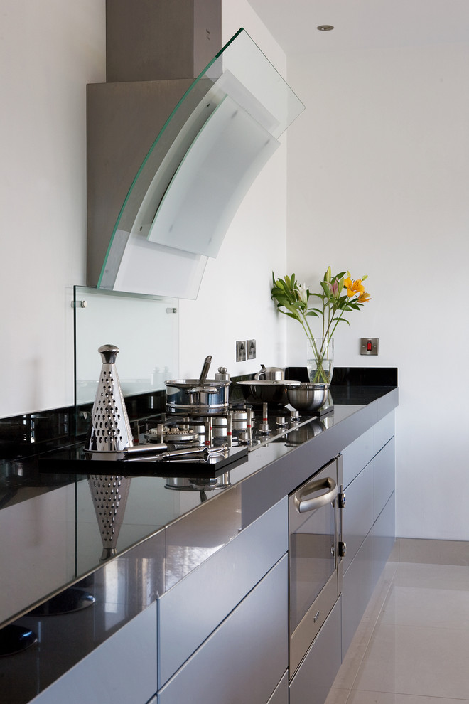 Moderne Küche mit Küchengeräten aus Edelstahl, flächenbündigen Schrankfronten und Glasrückwand in Sonstige
