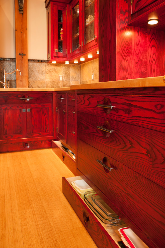 Example of a mid-sized mountain style l-shaped bamboo floor and beige floor open concept kitchen design in Seattle with a double-bowl sink, recessed-panel cabinets, red cabinets, soapstone countertops, brown backsplash, stone tile backsplash, paneled appliances and an island