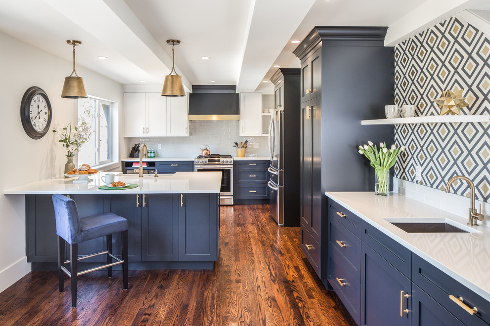 Inspiration for a medium sized classic l-shaped open plan kitchen in Vancouver with a belfast sink, shaker cabinets, blue cabinets, engineered stone countertops, grey splashback, metro tiled splashback, stainless steel appliances, medium hardwood flooring, a breakfast bar and brown floors.