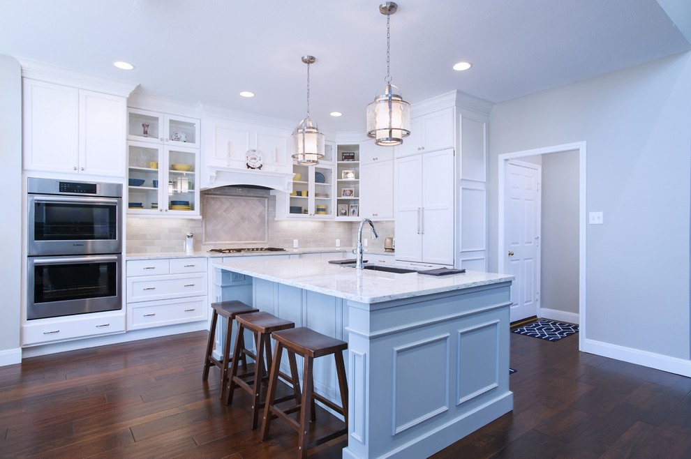 Inredning av ett klassiskt vit vitt kök, med en undermonterad diskho, luckor med infälld panel, blå skåp, grått stänkskydd, stänkskydd i tunnelbanekakel, integrerade vitvaror, mellanmörkt trägolv, en köksö och brunt golv