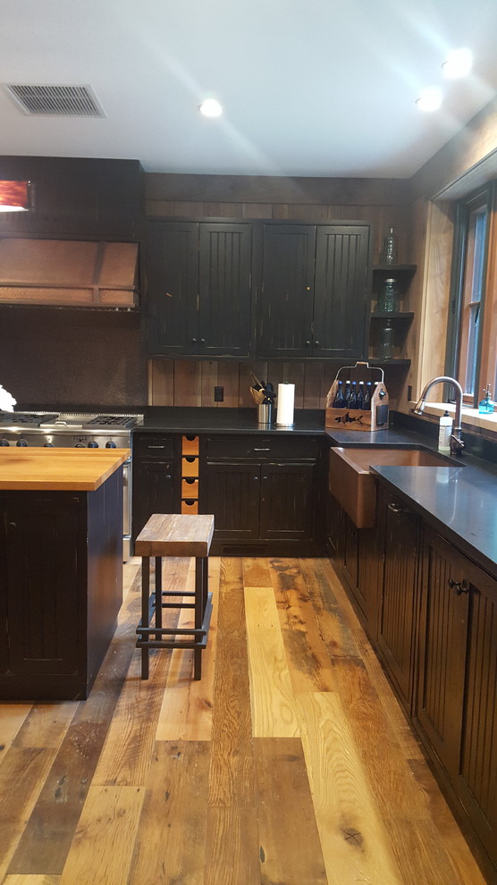 Immagine di una grande cucina rustica con ante a filo, ante nere, top in granito, paraspruzzi beige, elettrodomestici in acciaio inossidabile, pavimento in legno massello medio e pavimento marrone