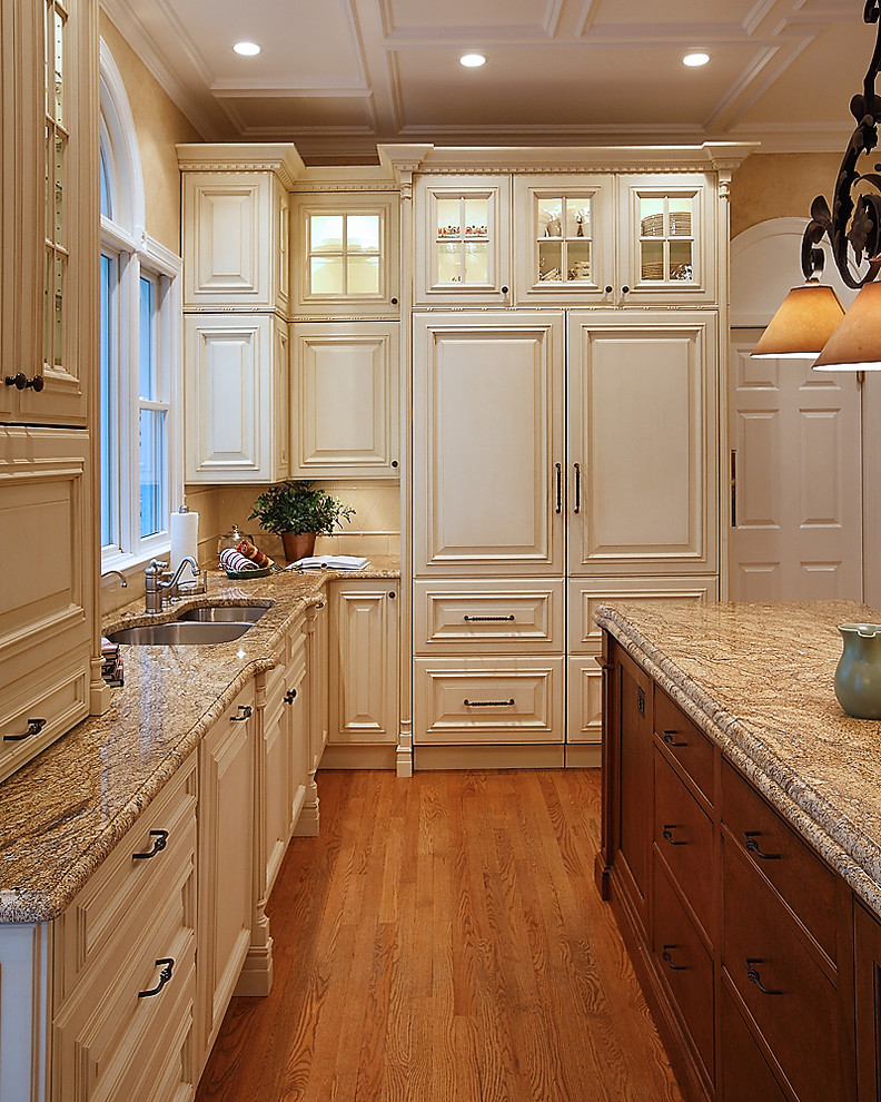 Exempel på ett stort klassiskt kök, med en dubbel diskho, luckor med upphöjd panel, beige skåp, granitbänkskiva, integrerade vitvaror, mellanmörkt trägolv och en köksö