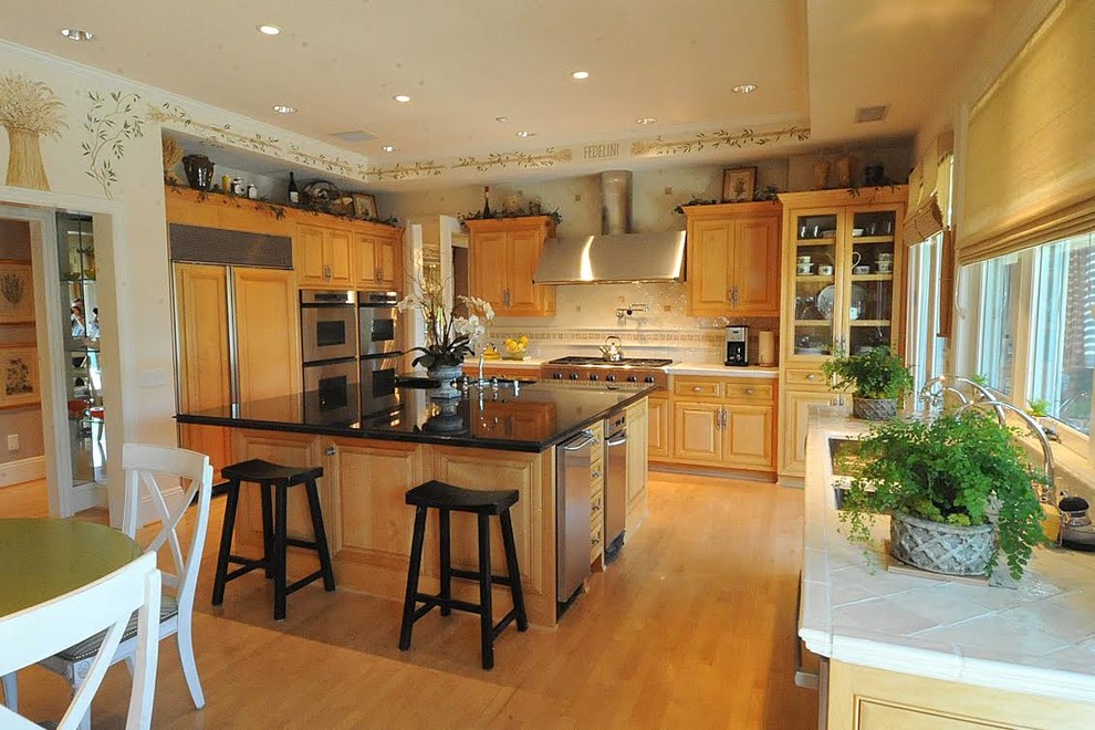 Klassisk inredning av ett mellanstort kök, med en undermonterad diskho, luckor med upphöjd panel, skåp i mellenmörkt trä, kaklad bänkskiva, beige stänkskydd, stänkskydd i porslinskakel, rostfria vitvaror, ljust trägolv, en köksö och brunt golv