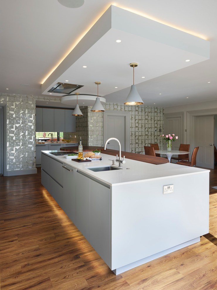 Photo of a contemporary kitchen in Buckinghamshire with a submerged sink, flat-panel cabinets, white cabinets, medium hardwood flooring and an island.