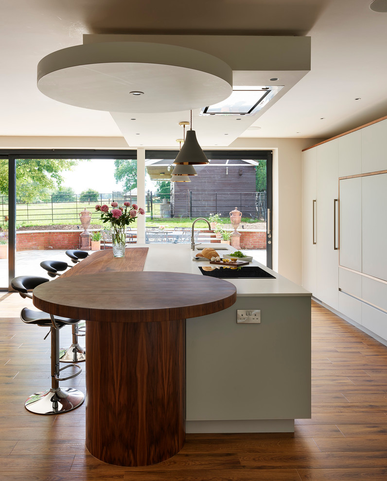 Moderne Küche mit Unterbauwaschbecken, flächenbündigen Schrankfronten, weißen Schränken, braunem Holzboden und Kücheninsel in Buckinghamshire