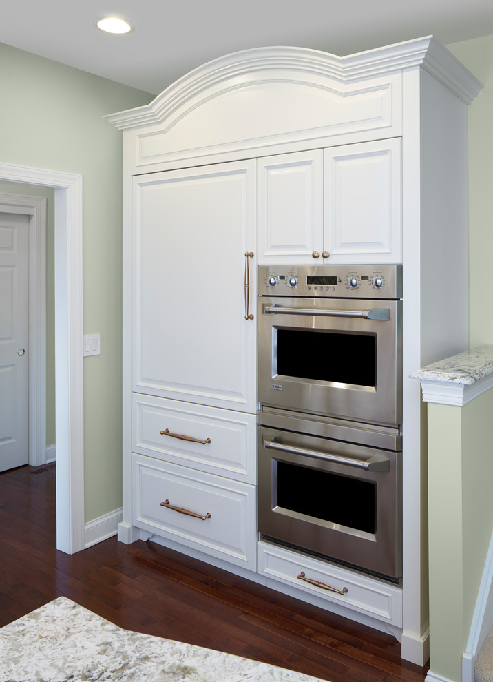 Inredning av ett klassiskt stort kök, med en undermonterad diskho, luckor med upphöjd panel, vita skåp, granitbänkskiva, beige stänkskydd, stänkskydd i keramik, integrerade vitvaror, mellanmörkt trägolv och en köksö