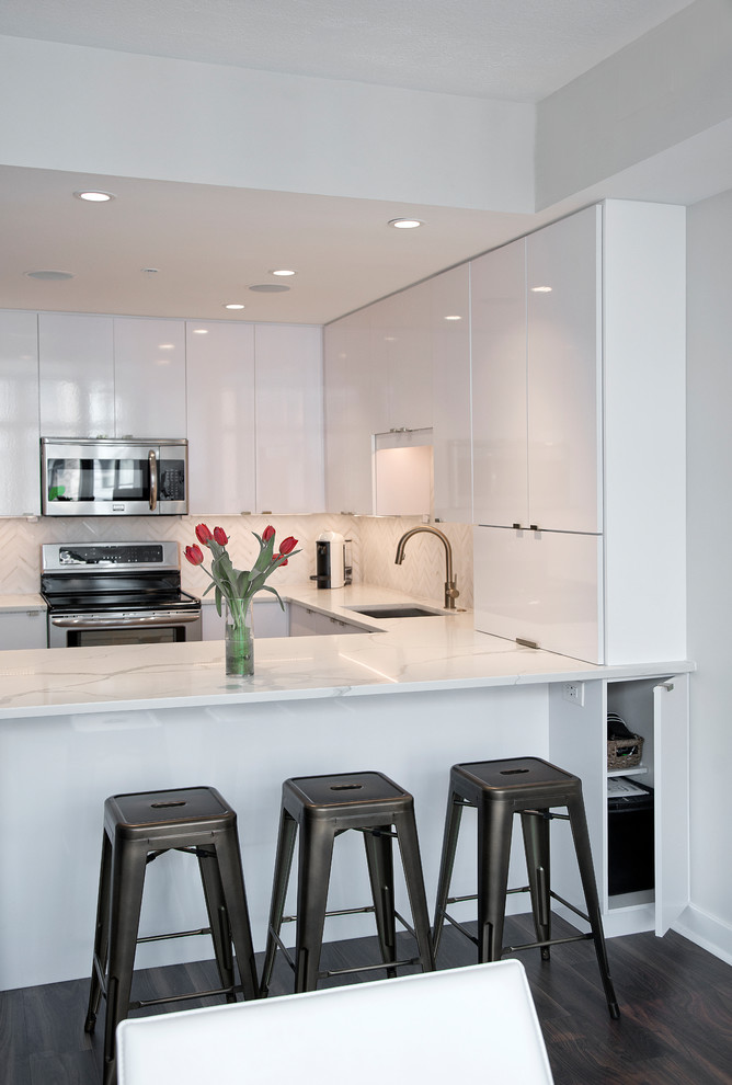 This is an example of a modern single-wall kitchen/diner in DC Metro with a submerged sink, flat-panel cabinets, white cabinets, engineered stone countertops, white splashback, stainless steel appliances, dark hardwood flooring, a breakfast bar, brown floors and white worktops.