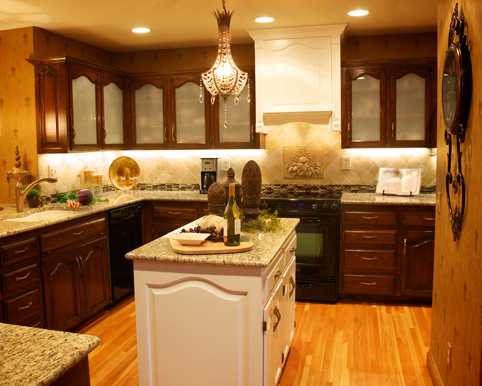 Bild på ett mellanstort vintage kök, med en undermonterad diskho, luckor med glaspanel, skåp i mörkt trä, granitbänkskiva, beige stänkskydd, stänkskydd i stenkakel, svarta vitvaror, ljust trägolv och en köksö