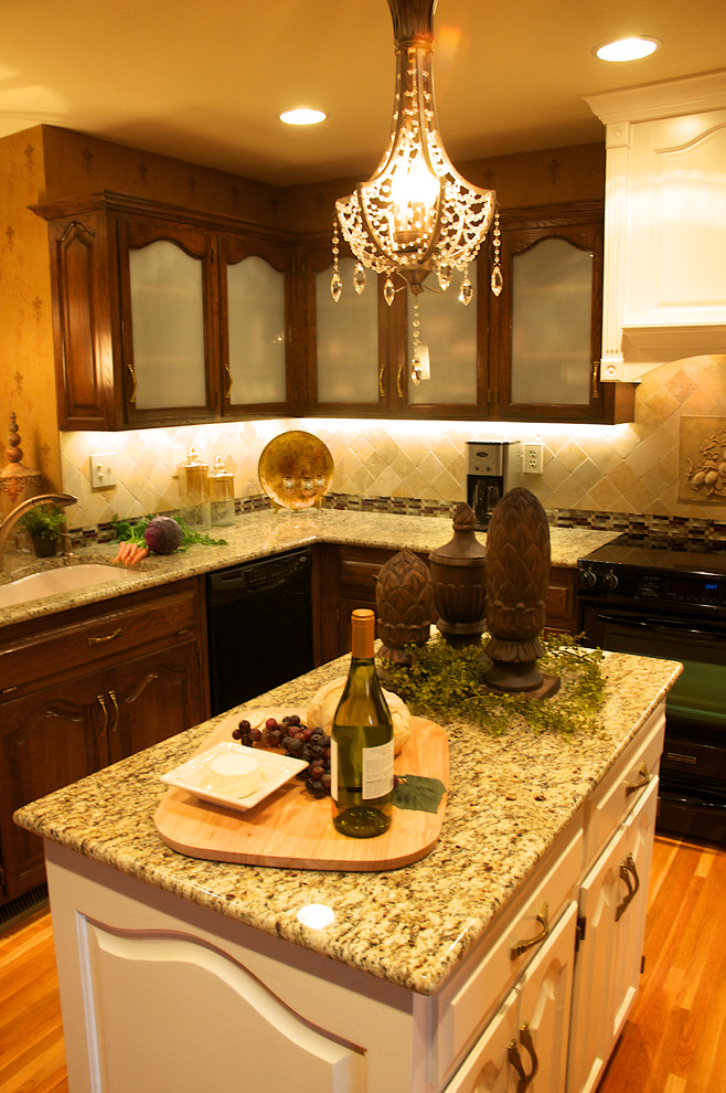 Esempio di una cucina chic di medie dimensioni con lavello sottopiano, ante di vetro, ante in legno bruno, top in granito, paraspruzzi beige, paraspruzzi con piastrelle in pietra, elettrodomestici neri e parquet chiaro