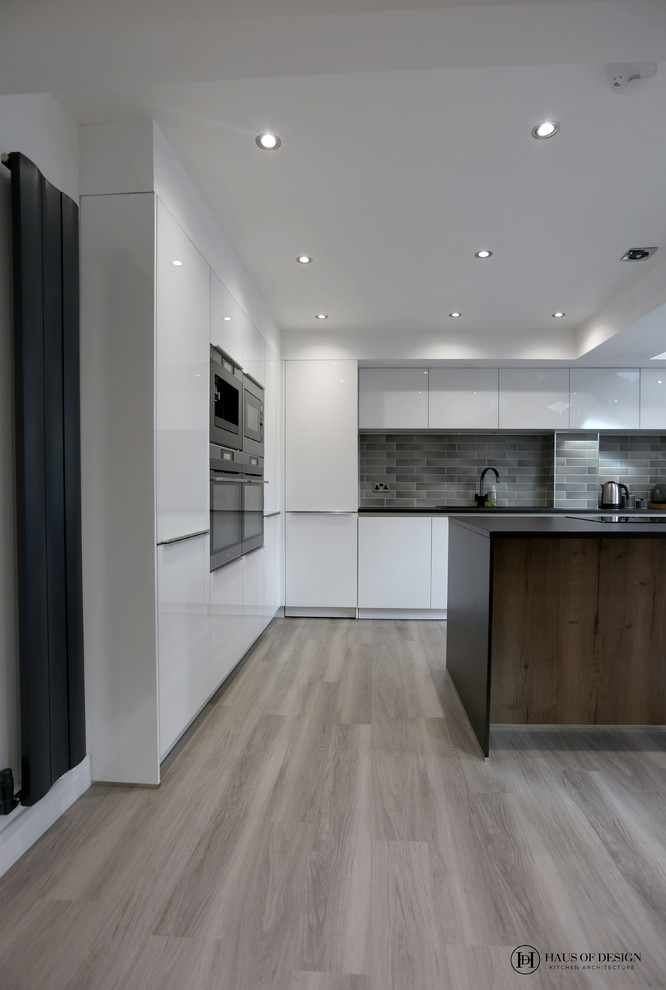 This is an example of a medium sized modern l-shaped open plan kitchen in Other with an integrated sink, flat-panel cabinets, white cabinets, laminate countertops, grey splashback, ceramic splashback, black appliances, medium hardwood flooring, an island, grey floors and black worktops.