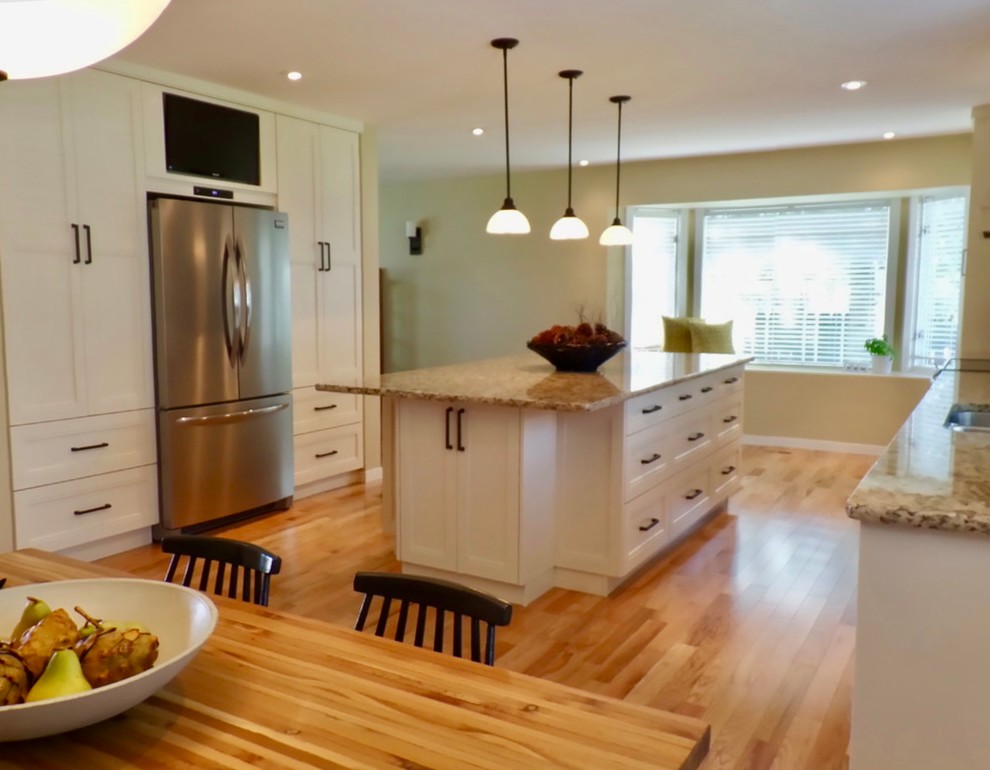 Example of a large classic galley light wood floor eat-in kitchen design in Calgary with a double-bowl sink, flat-panel cabinets, white cabinets, granite countertops, beige backsplash, glass tile backsplash, stainless steel appliances and an island