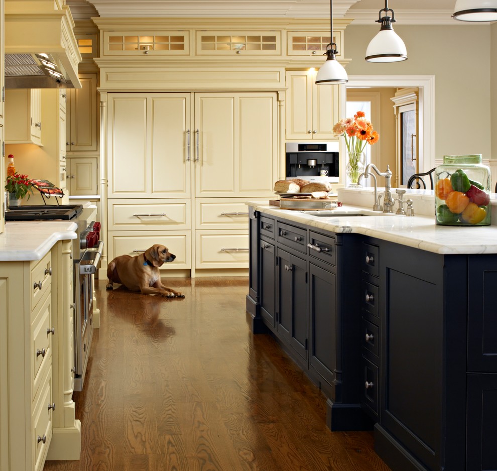 Foto på ett mellanstort vintage kök, med luckor med upphöjd panel, beige skåp, integrerade vitvaror, en undermonterad diskho, marmorbänkskiva, mellanmörkt trägolv och en köksö