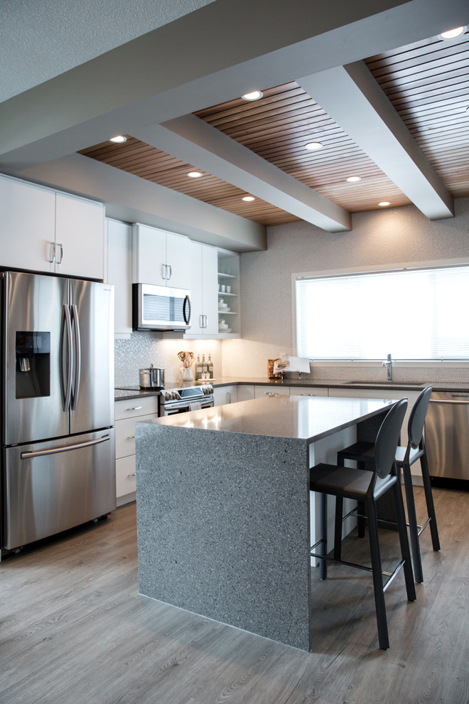 This is an example of a medium sized traditional u-shaped kitchen in Calgary with a submerged sink, flat-panel cabinets, white cabinets, white splashback, mosaic tiled splashback, stainless steel appliances, vinyl flooring and an island.