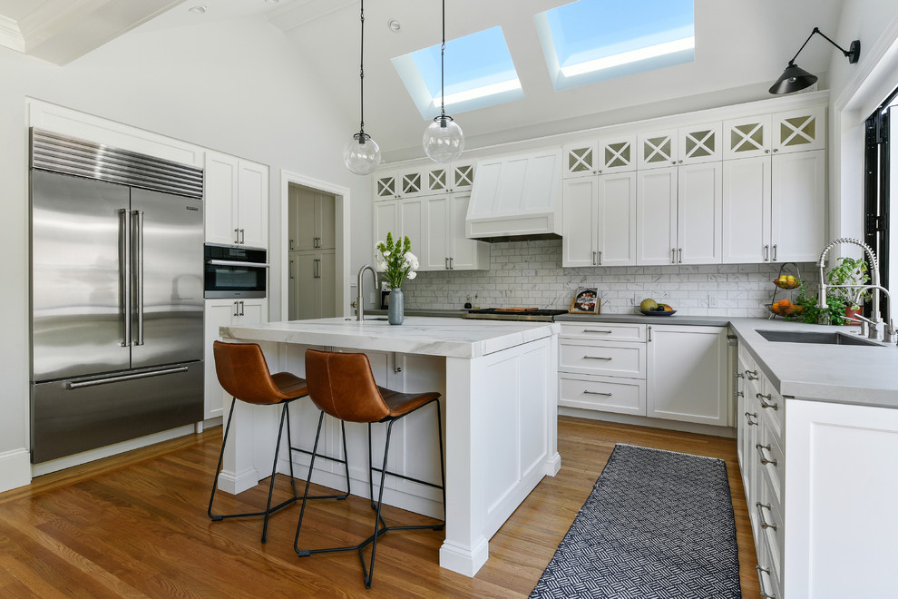 Inredning av ett klassiskt mellanstort grå grått kök, med en undermonterad diskho, skåp i shakerstil, vita skåp, bänkskiva i betong, vitt stänkskydd, stänkskydd i marmor, rostfria vitvaror, mellanmörkt trägolv, en köksö och brunt golv