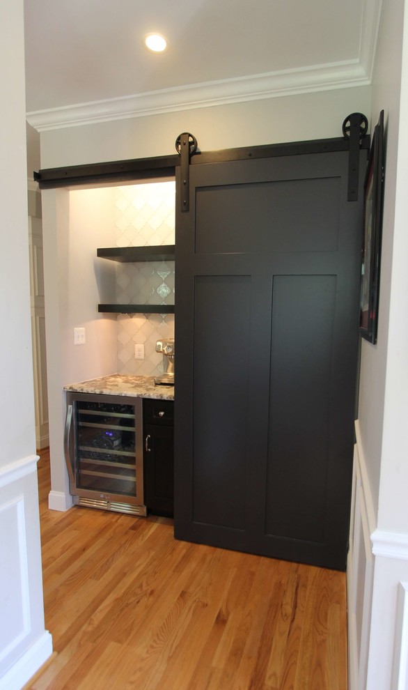 Klassisk inredning av ett stort grå grått kök, med en rustik diskho, luckor med infälld panel, granitbänkskiva, vitt stänkskydd, stänkskydd i glaskakel, rostfria vitvaror, ljust trägolv, en köksö, brunt golv och vita skåp