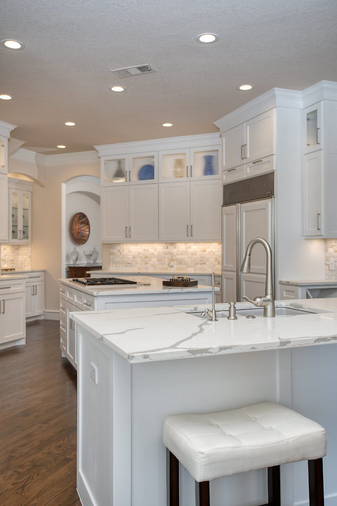 Large transitional u-shaped medium tone wood floor and brown floor open concept kitchen photo in Dallas with a double-bowl sink, shaker cabinets, white cabinets, quartz countertops, white backsplash, marble backsplash, stainless steel appliances, two islands and white countertops