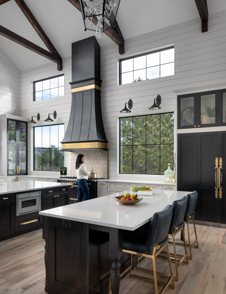 Eat-in kitchen - cottage light wood floor and beige floor eat-in kitchen idea in Other with glass-front cabinets, black cabinets, granite countertops, beige backsplash, stone tile backsplash, black appliances, two islands and white countertops