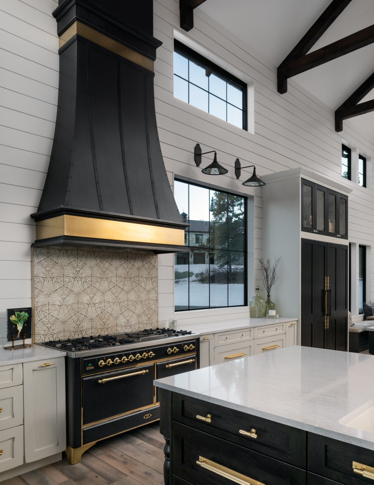Foto på ett lantligt vit kök och matrum, med luckor med glaspanel, svarta skåp, granitbänkskiva, beige stänkskydd, stänkskydd i stenkakel, svarta vitvaror, ljust trägolv, flera köksöar och beiget golv
