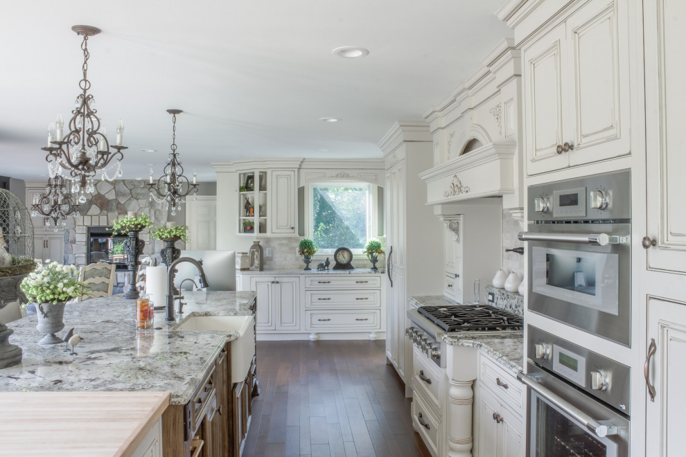 Large elegant l-shaped medium tone wood floor and brown floor eat-in kitchen photo in Detroit with a farmhouse sink, raised-panel cabinets, distressed cabinets, quartz countertops, beige backsplash, marble backsplash, stainless steel appliances, an island and white countertops