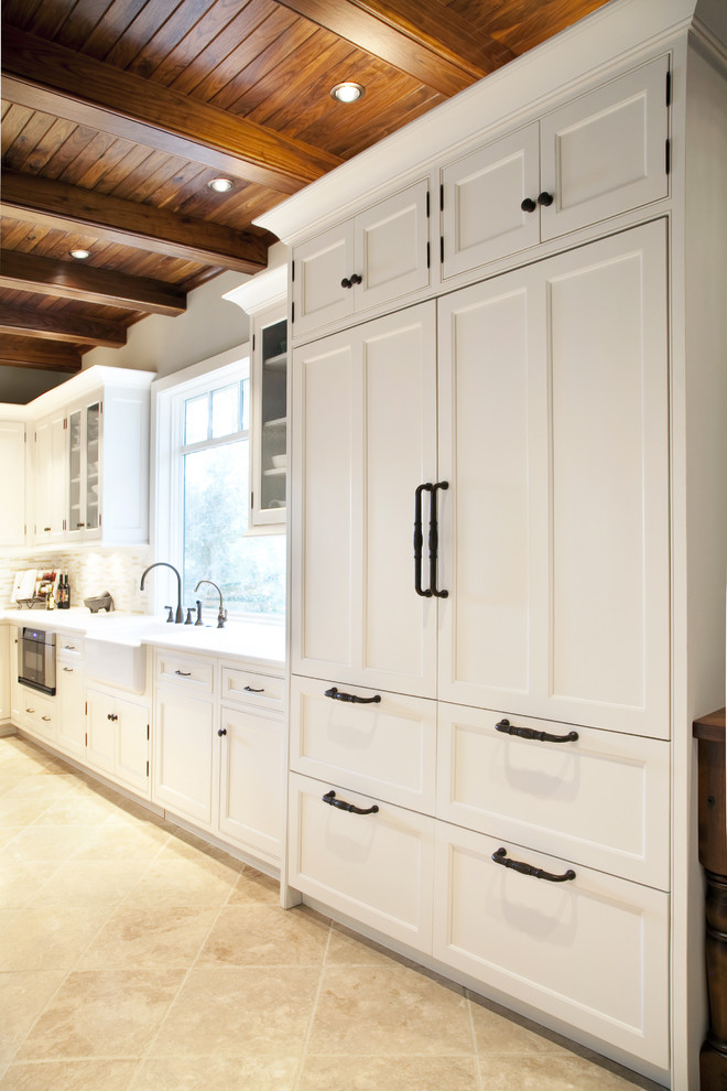 Example of a mid-sized classic u-shaped limestone floor eat-in kitchen design in Charleston with a farmhouse sink, shaker cabinets, white cabinets, marble countertops, beige backsplash, matchstick tile backsplash, stainless steel appliances and an island