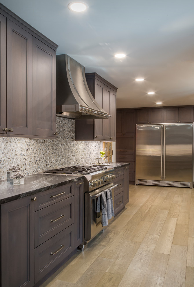 This is an example of a large contemporary galley kitchen pantry in Other with recessed-panel cabinets, brown cabinets, marble worktops, metallic splashback, mosaic tiled splashback, stainless steel appliances, light hardwood flooring, beige floors and black worktops.
