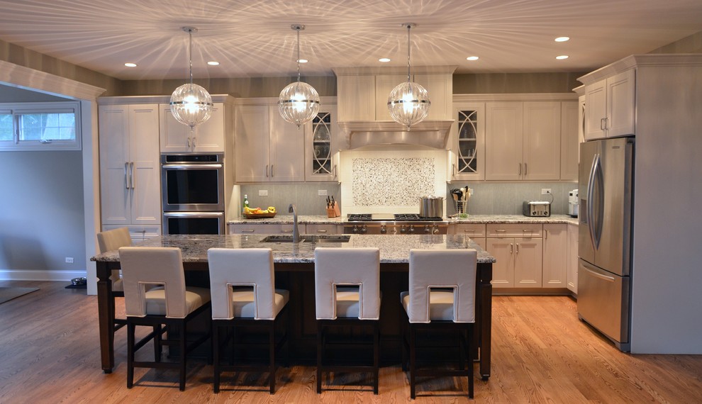 Example of a large transitional l-shaped medium tone wood floor open concept kitchen design in Other with an undermount sink, recessed-panel cabinets, white cabinets, granite countertops, gray backsplash, mosaic tile backsplash, stainless steel appliances and an island