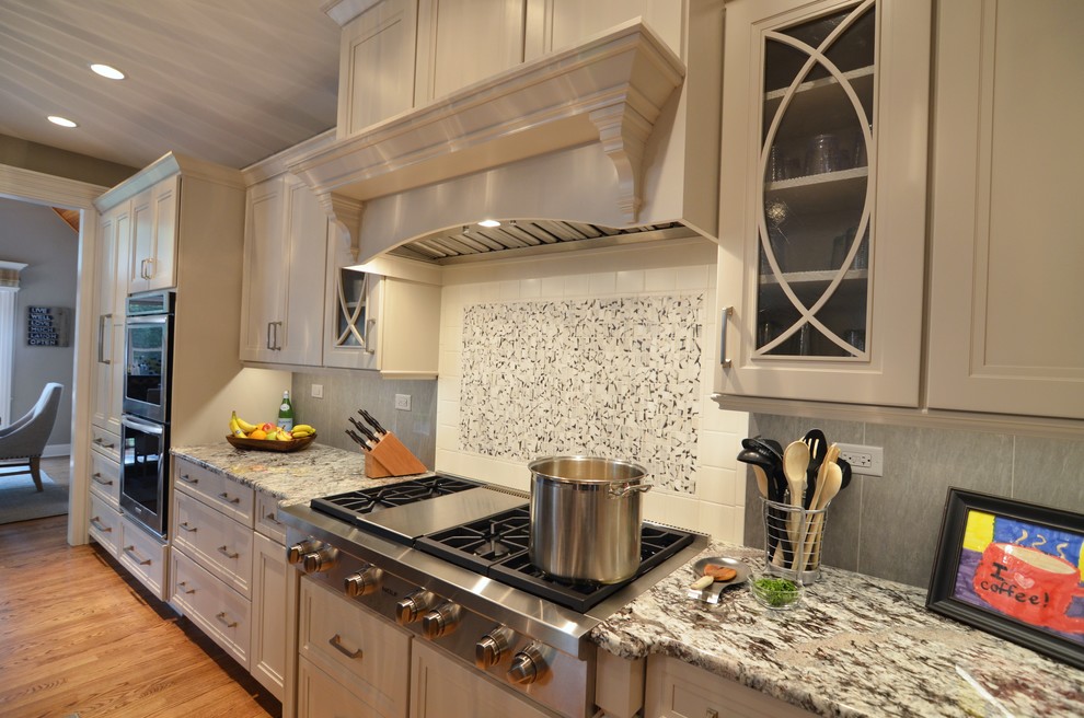 Example of a large transitional l-shaped medium tone wood floor open concept kitchen design in Other with an undermount sink, recessed-panel cabinets, white cabinets, granite countertops, gray backsplash, mosaic tile backsplash, stainless steel appliances and an island