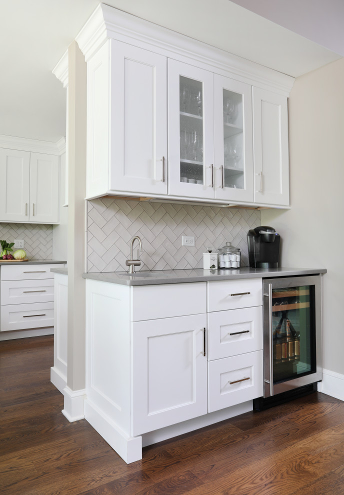 Klassisk inredning av ett grå grått kök, med en undermonterad diskho, vita skåp, grått stänkskydd, stänkskydd i keramik, en köksö, brunt golv, luckor med infälld panel, bänkskiva i kvartsit, rostfria vitvaror och mellanmörkt trägolv