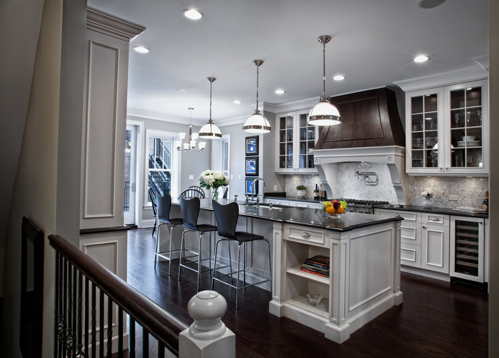 Photo of a large traditional galley kitchen/diner in Chicago with glass-front cabinets, white cabinets, white splashback, integrated appliances, a submerged sink, granite worktops, stone tiled splashback, dark hardwood flooring and an island.