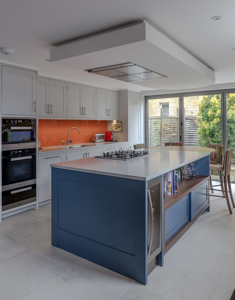 Eat-in kitchen - transitional galley gray floor eat-in kitchen idea in London with shaker cabinets, gray cabinets, orange backsplash, black appliances and an island