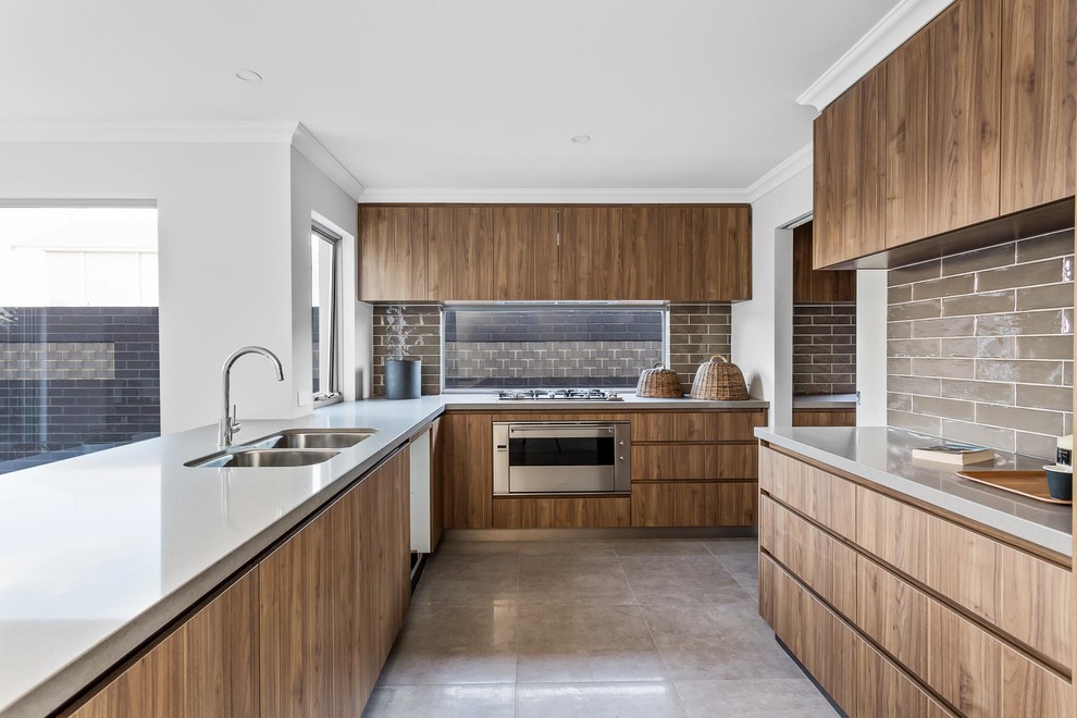 Modern inredning av ett kök, med en dubbel diskho, släta luckor, skåp i mellenmörkt trä, brunt stänkskydd, stänkskydd i glaskakel, rostfria vitvaror, en halv köksö och beiget golv